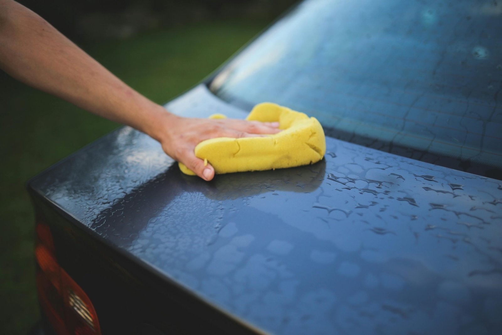 man-hand-car-black-6003 Hand cleaning car with a yellow sponge, showcasing car detailing and washing process.