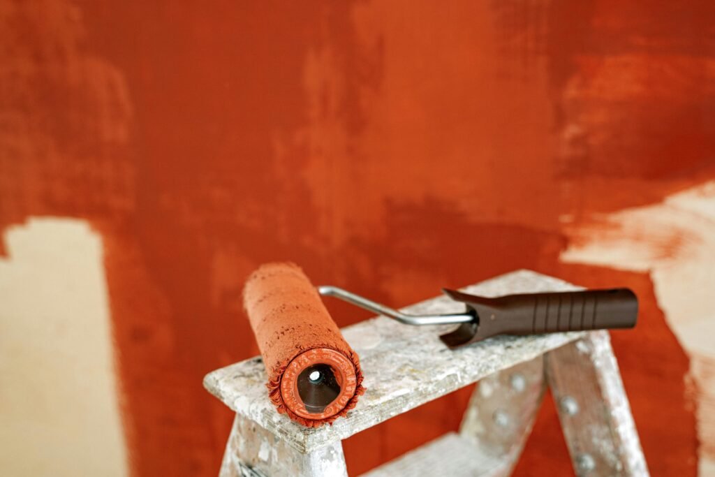 Close-up of a paint roller resting on a stepladder against a partially painted wall.